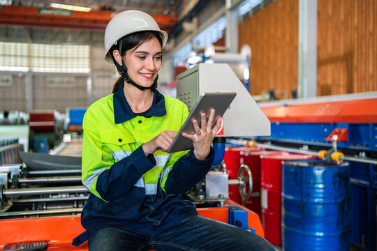 Professional machanic engineer technician industrial woman wearing safety uniform working control with tablet on heavy machine in manufacturing factory production line.business technology robot