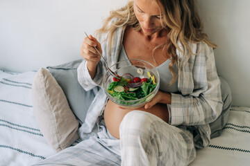 A pregnant woman eats green fresh vegetable salad taking care of her health.