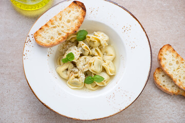 Plate of italian tortellini in brodo on a beige granite background, high angle view, horizontal shot