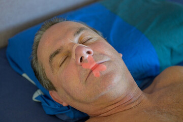 Sleeping middle aged man with a nose tape and a red mouth tape