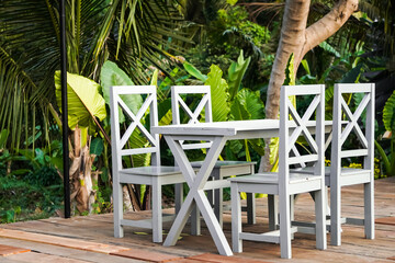 Cafe tables and chairs set made of solid wood against outdoors garden and wooden floor background....