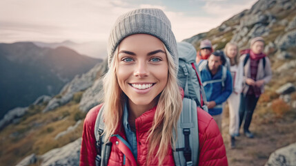 Fototapeta premium a Smiling young woman hiker with backpack looking at camera with group of friends hikers rises to the top of the hill. Hiker, Tourist camp. Generative Ai