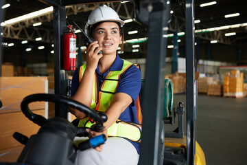 Indian worker driving a forklift and using walkie talkie in warehouse storage