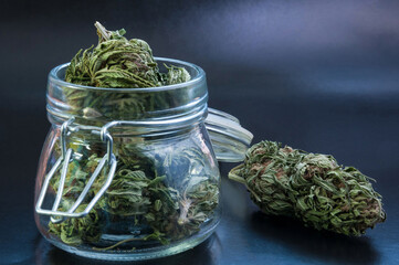 noir still life with glass mason jar full of medical cannabis buds on black background