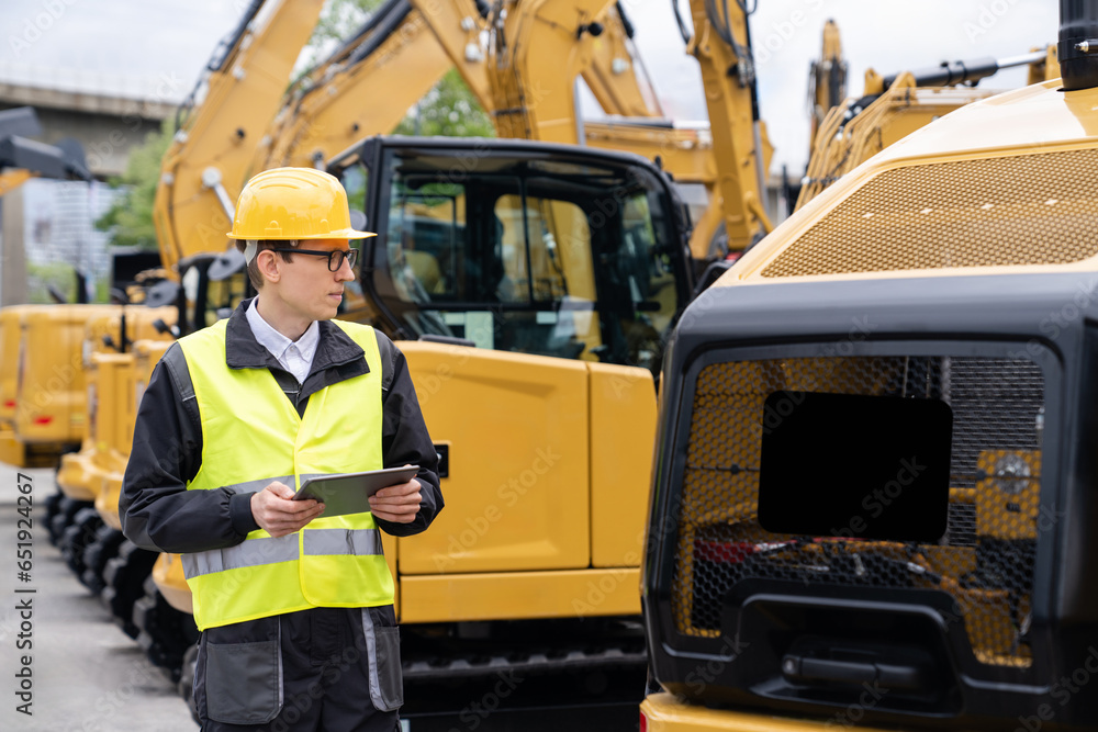 Aufkleber engineer in a helmet with a digital tablet stands next to construction excavators.