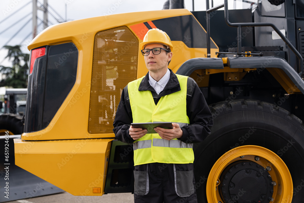 Aufkleber Worker in a helmet with a digital tablet on the background of construction machine