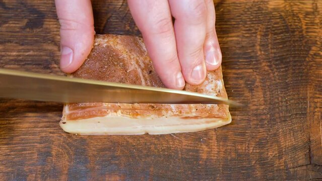 Slicing of salted pork fatback on cutting board, close-up. Ukrainian traditional food - salo