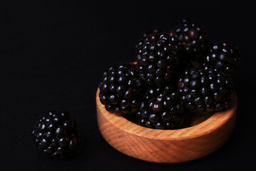 Wooden bowl of blackberries on black table with black background.