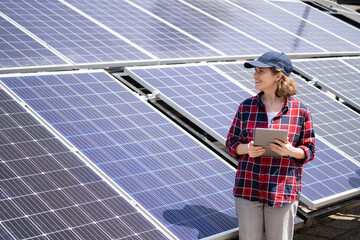 Woman with digital tablet stands next to solar panel.