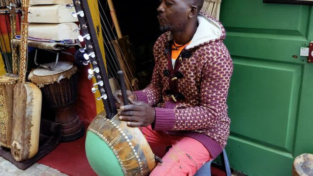 A Senegalese man plays a traditional kora string instrument. Traditional Afro-African music is often played in the streets, at weddings, and at festivals. 4k footage.
