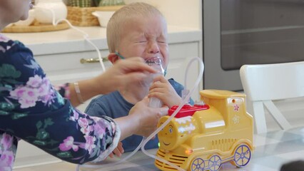 sick child crying while doing inhalation mother using nebulizer helps little boy do inhalation