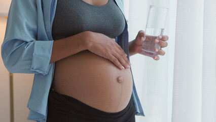 Woman tenderly caressing baby bump while sipping water
