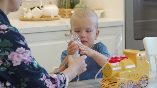 sick child crying while doing inhalation mother using nebulizer helps little boy do inhalation