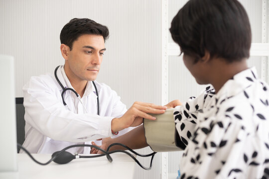 Hispanic doctor measuring African American patient's blood pressure. Person medical healthcare and wellbeing, the physician meet with patient at clinic concept.