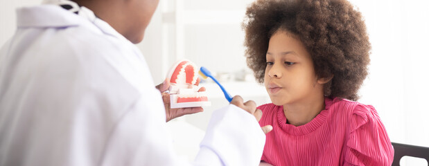 African American dentist explaining to mixed-race afro child how to brush teeth. The doctor and...