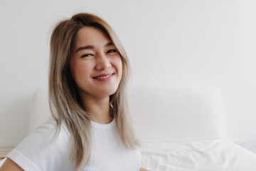 Naklejka premium Asian woman smiling and looking at camera , wearing white top and sitting sofa at home alone with happy life.