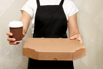a woman cafe worker holds out a box with ready-made pizza and a cup of coffee