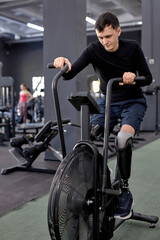 Fototapeta na wymiar slim fit guy using stationary bike at sport center, full length shot