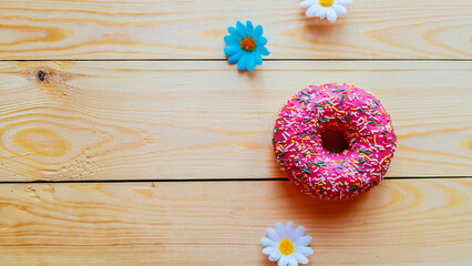 Strawberry donut with colorful sprinkles on wooden background, copy space
