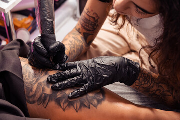 Professional tattooist creating black and white flower design on female thigh - obrazy, fototapety, plakaty