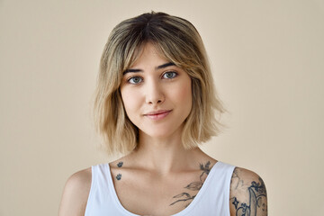 Young blond pretty smiling girl beauty female model with short blonde hair beautiful face healthy skin and tattoos looking at camera isolated at beige background. Close up headshot portrait.