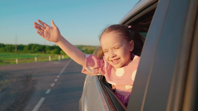 Child, stretching his hand out of car window, laughs. Girl child looks out of car window. Happy family travels by car. Little girl rejoices in family train by car. Childrens emotions. Family vacation