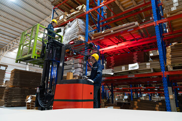 Male warehouse worker using forklift electric or electric pallet stacker lift lifting female colleague to check cardboard boxes or corrugated paper sheet goods on shelves in store warehouse. © Supachai