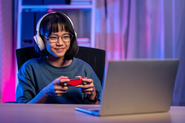 Young asian woman enjoy playing video game by talking on headphones in living room at night.