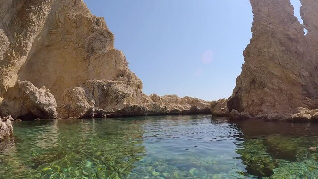 Panorama of beautiful rocky bay in Mediterranean Sea at Stegna beach, Rhodes island, Greece. A woman standing in water inspects coastal rocks, slow motion
