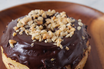 Close up detail shot of delicious sweet chocolate glazed donut with cashew nut served on wooden plate. Isolated image on white background