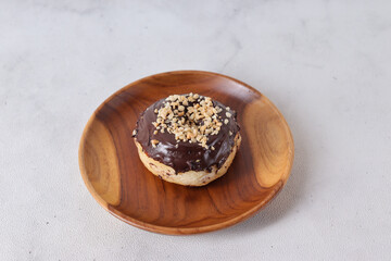 Delicious sweet chocolate glazed donut with cashew nut served on wooden plate. Isolated image on white background