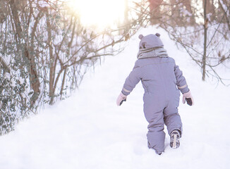 Fototapeta na wymiar A little girl is walking in the park on the snow winter day.