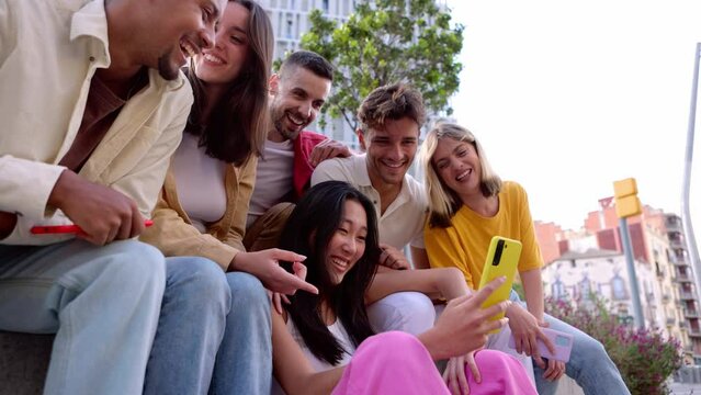 Young group of gen z people having fun using cell phone together outside. Cheerful community of student zoomers enjoying social media content on smartphone app.