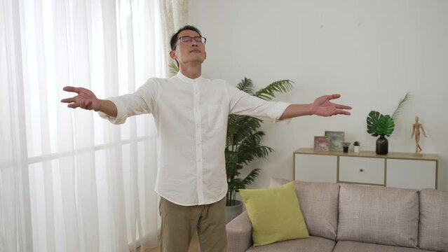slow motion of asian Japanese mature man relaxing calming himself by spreading arms and breathing deep and slow in the living room at home with daylight.
