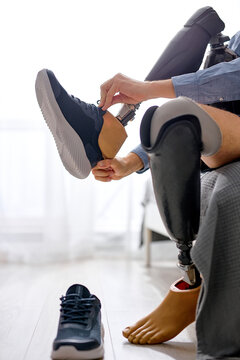 cropped unrecognizable handicapped man leg amputee wearing sneakers on prosthesis at home sitting on bed, handicapped difficulties after accident injures. guy preparing for the day