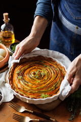 Warm baked spiral tart with colorful vegetables cut into strips in a baking dish placed on the table, focus on the center of the tart.