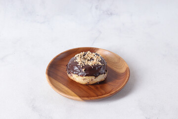 Delicious sweet chocolate glazed donut with cashew nut served on wooden plate. Isolated image on white background