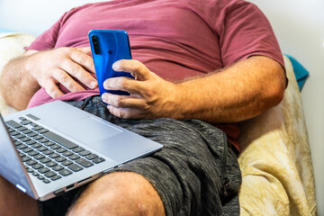 Unrecognizable person. Sedentary overweight man, sitting eating pastries next to a phone and a...