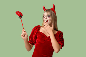 Surprised young woman dressed for Halloween as devil with trident on green background