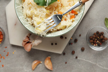 Board with bowl of delicious sauerkraut and different spices on grey background