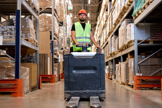 Forklift driver in warehouse. freight transport, Warehouse industrial delivery shipment, caucasian male pushing transport equipment, dressed in green uniform vest and safety helmet