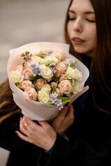 Attractive long haired girl gently holding delicate bouquet of light pink and creamy roses and looks on