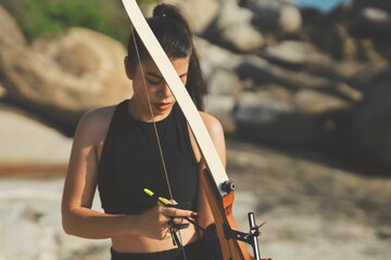 Smart young Asian Archery woman with bow shooting on the beach,sport girl.Asian woman in black...