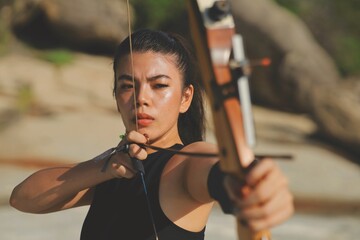 Smart young Asian Archery woman with bow shooting on the beach,sport girl.Asian woman in black under shirt holding Archery in hands.