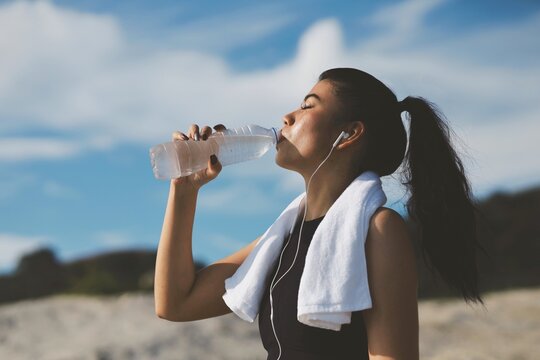 Beautiful woman drinking water after workout on the beach.