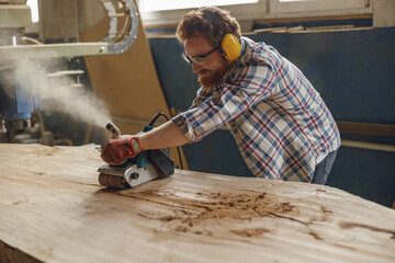 Professional male carpenter using electric sander for wood. Manufacture of wood products