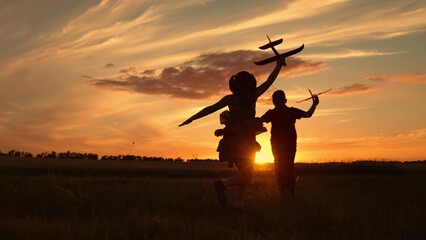 Children aviators boy girl run with toy plane across field in rays of sunset. Child wants to become an astronaut pilot. Children play with toy plane. Teenager dreams of flying, becoming pilot. Freedom
