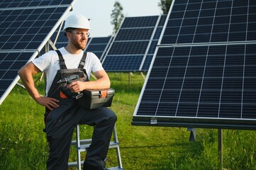 Side view of male worker installing solar modules and support structures of photovoltaic solar array. Electrician wearing safety helmet while working with solar panel. Concept of sun energy