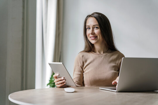 Employee manager is a person at work. Uses a laptop online website for the project and a desktop computer.  A young woman is smiling and working in the office daily routine.