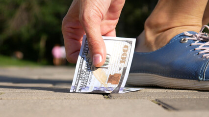 Close-up of a woman's hand picking up one hundred dollar bill on the sidewalk
